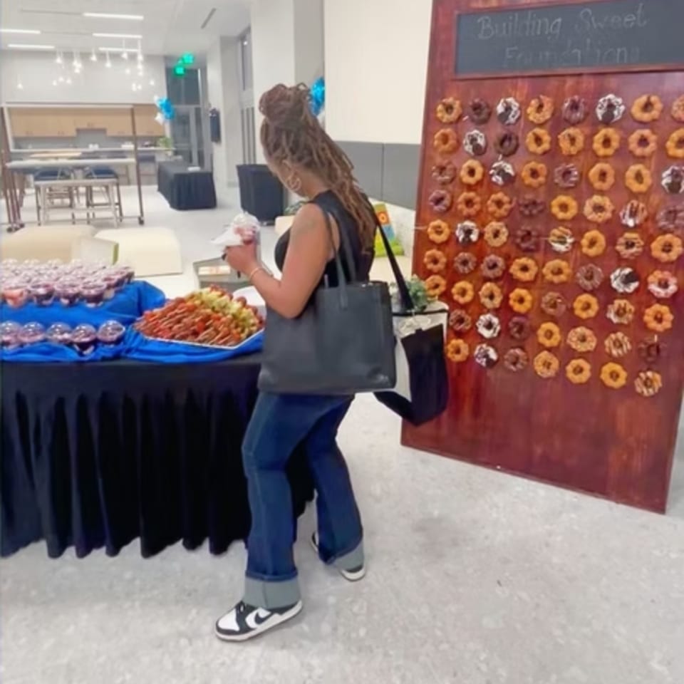 Woman browses pastries at a buffet table beside a colorful donut display in a bright indoor venue.