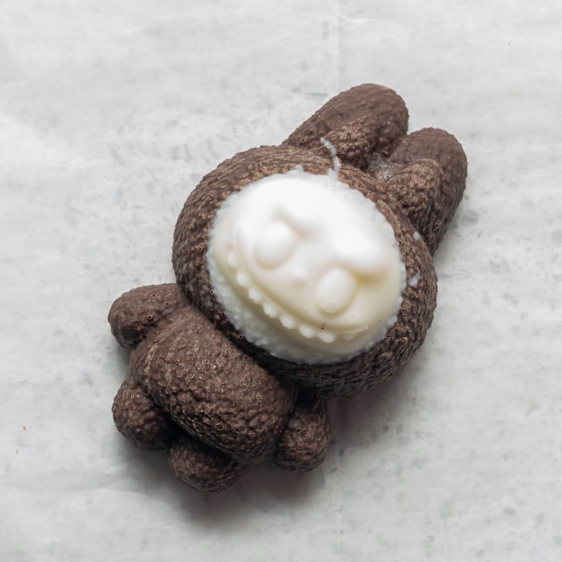 A chocolate bunny with a white chocolate face, detailed with eyes and a smile, on white parchment.