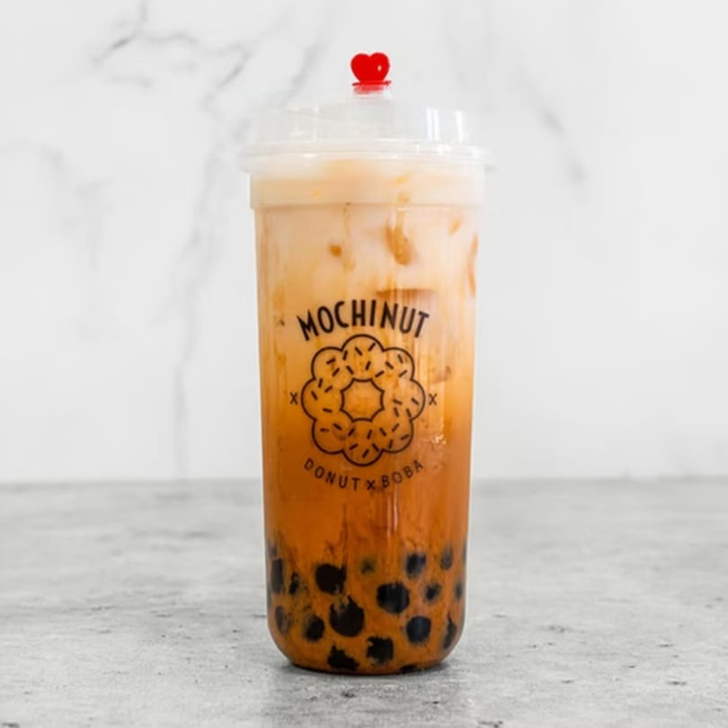 Mochinut Thai tea with boba in a clear cup with a red heart stopper.