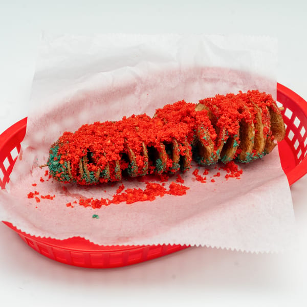 A spiral-cut potato on a stick, covered in red and green seasoning, in a red basket.