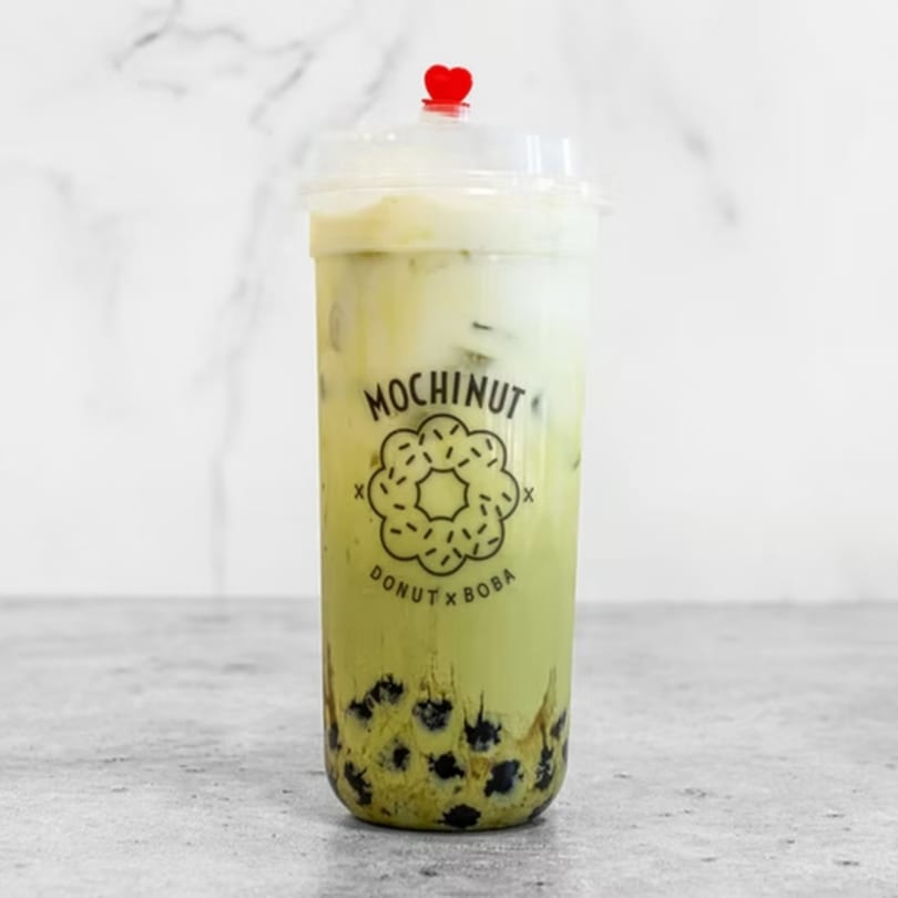 Mochinut matcha boba drink with a red heart stopper, on a white marble background.