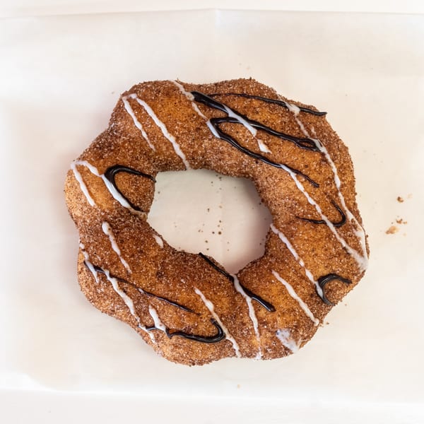 A cinnamon sugar churro donut with white and dark chocolate drizzle on a white background.