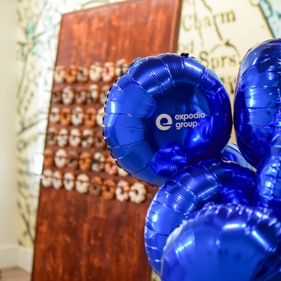 Blue Expedia Group balloons displayed beside a wooden sign covered with colorful lettering.