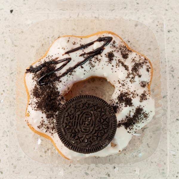 Overhead view of a white-frosted donut with chocolate drizzle and cookie crumbles, topped with an Oreo.