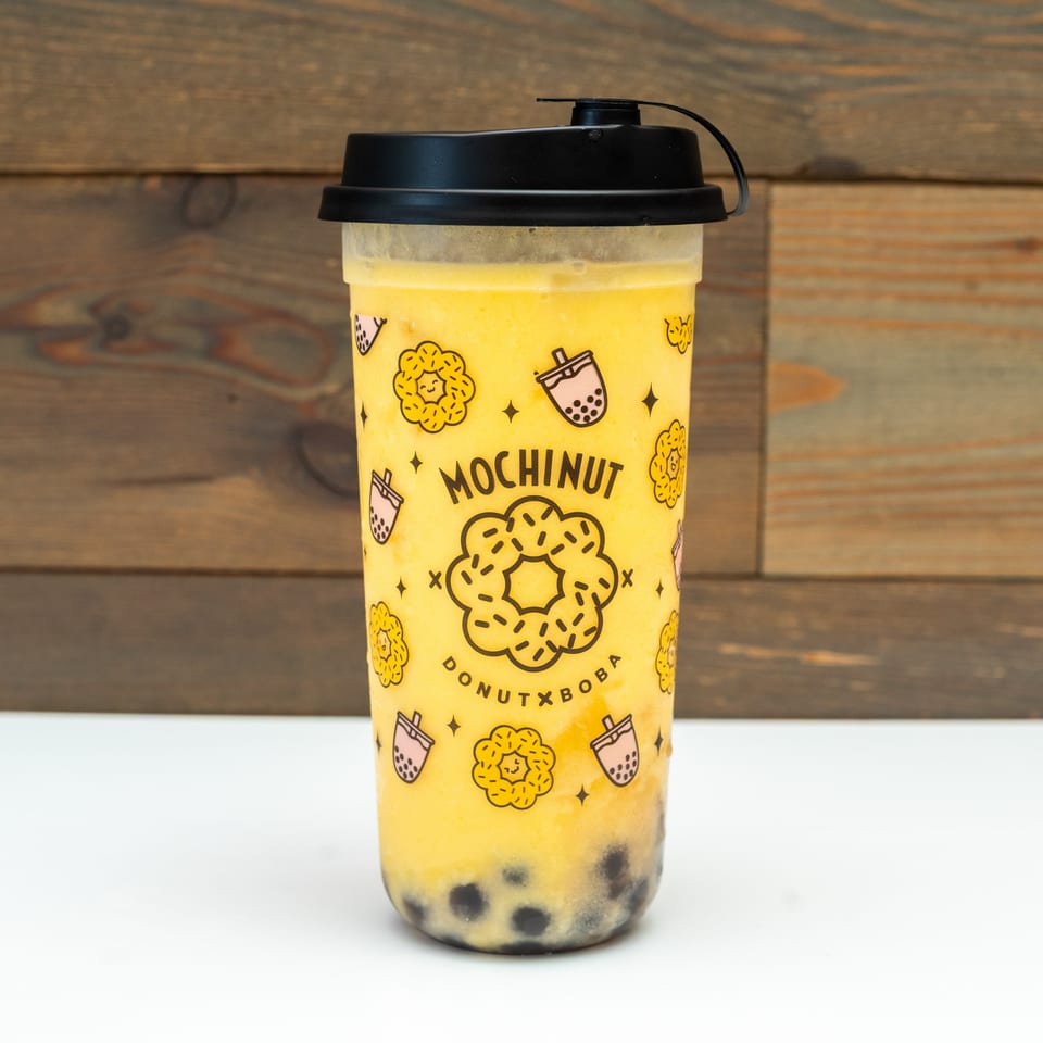 Mochinut mango boba drink with tapioca pearls, against a white and wooden background.